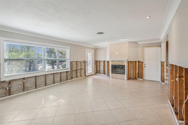 unfurnished living room with light tile patterned floors, a textured ceiling, ornamental molding, and a tiled fireplace