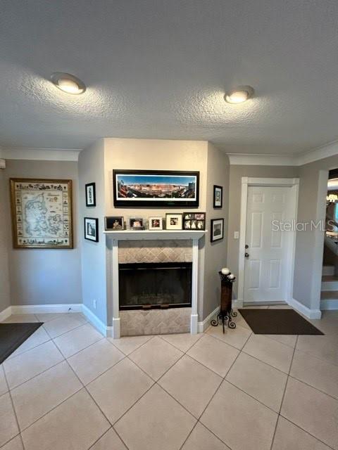 foyer entrance featuring a textured ceiling, light tile patterned floors, a fireplace, and ornamental molding