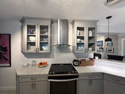 kitchen featuring wall chimney range hood, light stone counters, pendant lighting, gray cabinets, and stainless steel range with electric cooktop