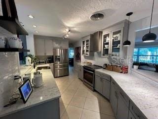 kitchen featuring gray cabinetry, wall chimney range hood, electric range, decorative light fixtures, and stainless steel fridge with ice dispenser