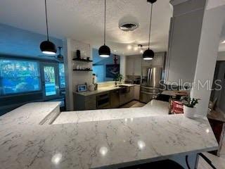 kitchen with decorative light fixtures, light stone counters, and kitchen peninsula