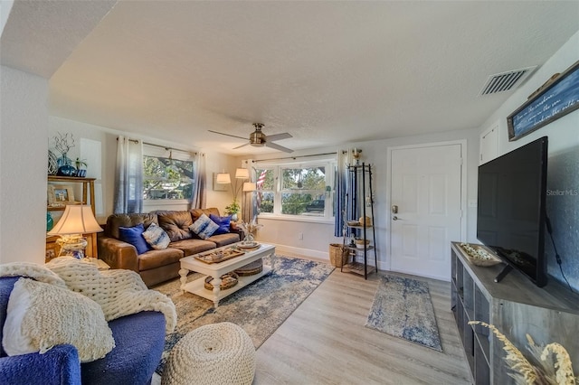 living room with ceiling fan, light wood-type flooring, and a textured ceiling