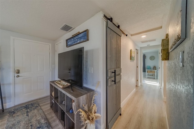 hallway with a barn door, light wood-type flooring, and a textured ceiling