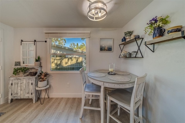 dining space with a barn door, a textured ceiling, and light wood-type flooring