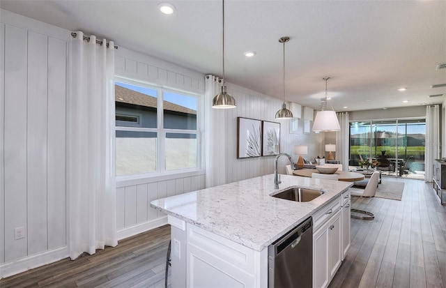 kitchen with pendant lighting, stainless steel dishwasher, sink, white cabinetry, and an island with sink