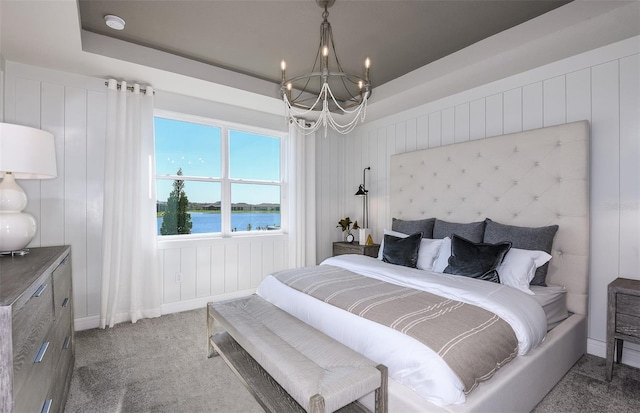 bedroom featuring carpet floors, wood walls, a chandelier, a water view, and a tray ceiling