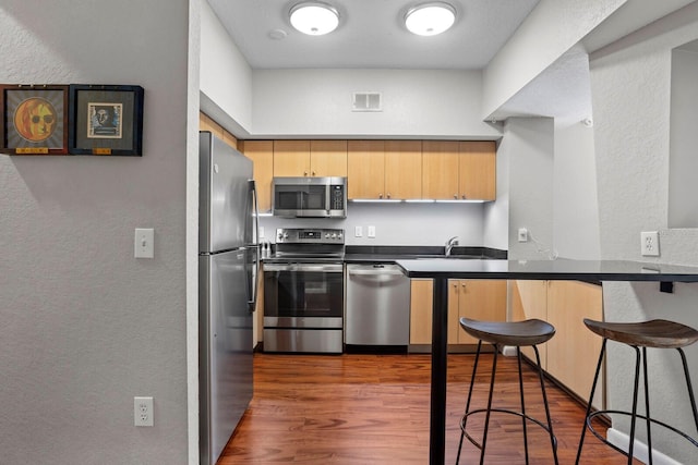 kitchen with a kitchen bar, appliances with stainless steel finishes, dark hardwood / wood-style flooring, sink, and light brown cabinets