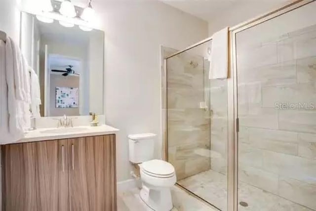 bathroom featuring vanity, toilet, a shower with door, and ceiling fan