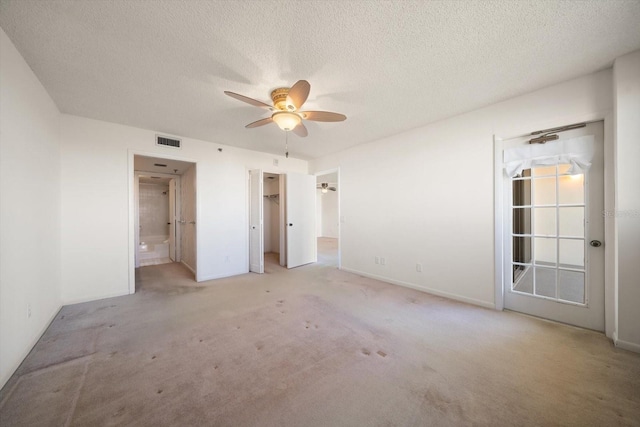 unfurnished bedroom with ensuite bath, ceiling fan, a spacious closet, and a textured ceiling