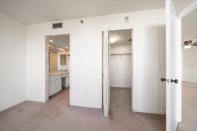 unfurnished bedroom featuring ensuite bathroom, a textured ceiling, a walk in closet, light carpet, and a closet