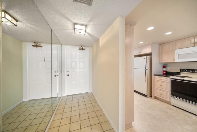 kitchen with a textured ceiling, white appliances, light tile patterned floors, and light brown cabinets