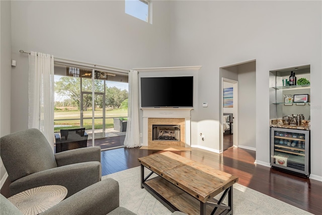 living room featuring beverage cooler, dark wood-type flooring, indoor bar, a fireplace, and a high ceiling