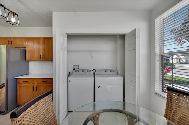 clothes washing area featuring light tile patterned floors, a textured ceiling, washer and clothes dryer, and plenty of natural light