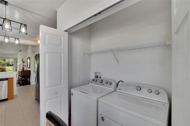 clothes washing area featuring light tile patterned flooring, washing machine and dryer, and a textured ceiling