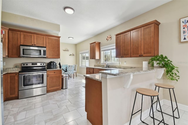 kitchen featuring a breakfast bar area, light tile patterned floors, light stone counters, kitchen peninsula, and stainless steel appliances