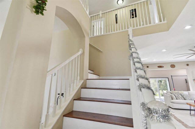 staircase with a towering ceiling and ceiling fan