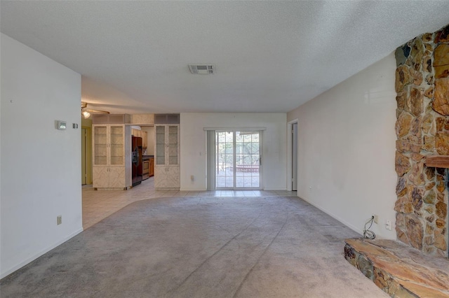 unfurnished living room featuring a stone fireplace, ceiling fan, light colored carpet, and a textured ceiling