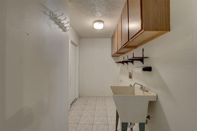 clothes washing area featuring cabinets, hookup for a washing machine, a textured ceiling, sink, and light tile patterned floors