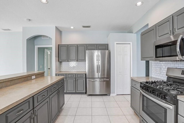 kitchen featuring gray cabinetry, decorative backsplash, stainless steel appliances, and light tile patterned flooring