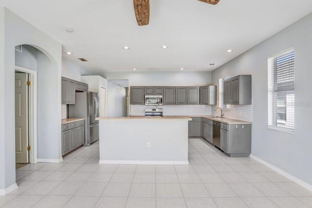 kitchen featuring sink, gray cabinetry, tasteful backsplash, appliances with stainless steel finishes, and a kitchen island