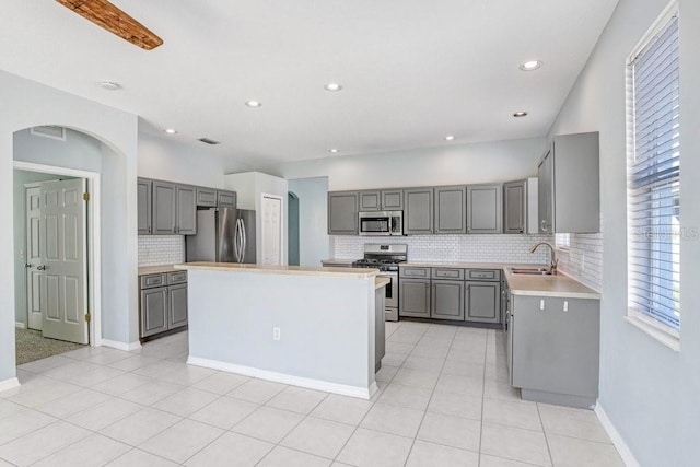 kitchen featuring light tile patterned floors, appliances with stainless steel finishes, gray cabinetry, a center island, and decorative backsplash