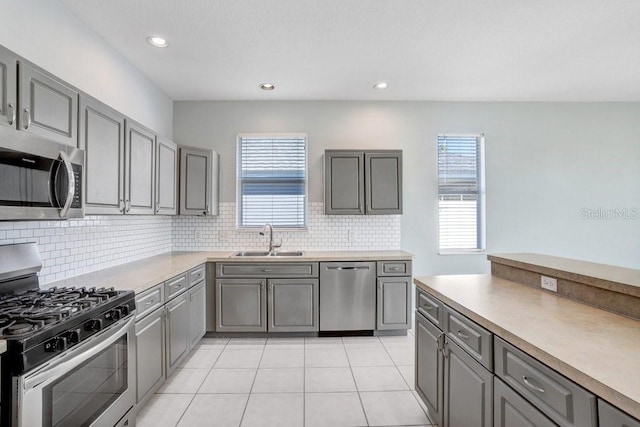 kitchen with sink, gray cabinetry, backsplash, light tile patterned floors, and stainless steel appliances