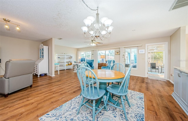 dining space with a textured ceiling, ceiling fan with notable chandelier, visible vents, and light wood-style floors