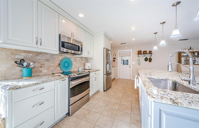 kitchen featuring pendant lighting, stainless steel appliances, tasteful backsplash, white cabinets, and a sink