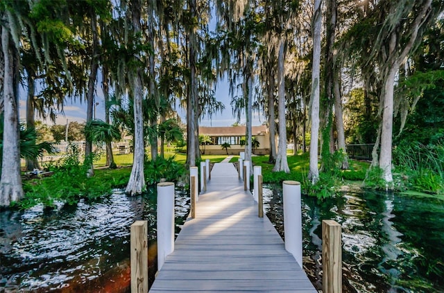 view of dock featuring a water view, fence, and a lawn