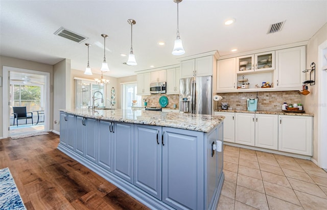 kitchen with a kitchen island with sink, visible vents, white cabinetry, appliances with stainless steel finishes, and glass insert cabinets