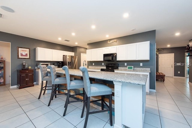 kitchen featuring white cabinets, a kitchen island with sink, a breakfast bar area, and black appliances