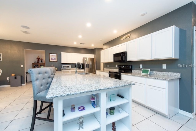 kitchen featuring black appliances, white cabinets, light stone countertops, light tile patterned floors, and an island with sink