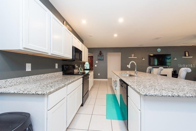 kitchen featuring a kitchen bar, sink, black appliances, a center island with sink, and white cabinetry