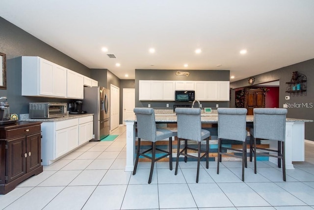 kitchen featuring stainless steel fridge, light stone countertops, a breakfast bar area, and a kitchen island with sink