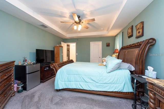 bedroom featuring a raised ceiling, stainless steel refrigerator, ceiling fan, and light carpet