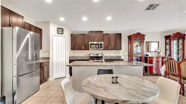 kitchen with decorative backsplash, stainless steel appliances, sink, an island with sink, and light tile patterned flooring