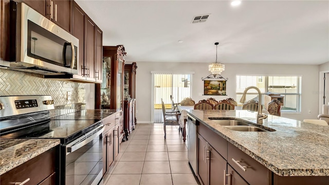 kitchen with a kitchen island with sink, sink, light tile patterned floors, appliances with stainless steel finishes, and tasteful backsplash