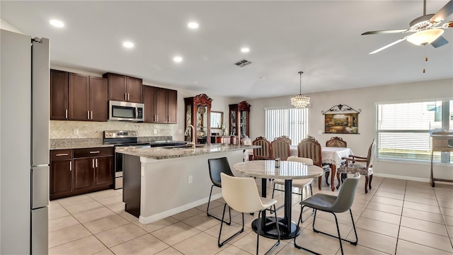 kitchen featuring light stone countertops, appliances with stainless steel finishes, sink, pendant lighting, and an island with sink