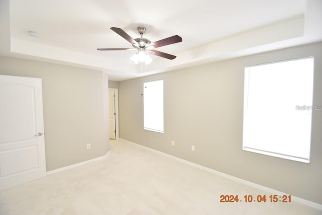 spare room featuring a tray ceiling, ceiling fan, and light colored carpet