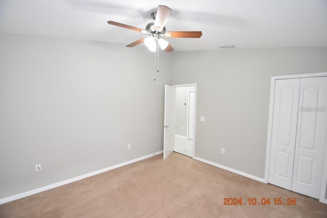 unfurnished bedroom featuring a closet, light colored carpet, vaulted ceiling, and ceiling fan