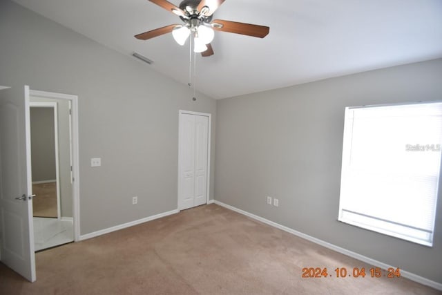 unfurnished bedroom featuring a closet, light colored carpet, vaulted ceiling, and ceiling fan