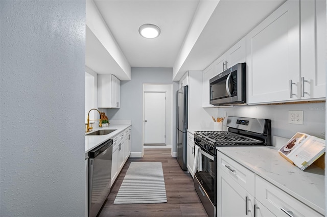 kitchen featuring appliances with stainless steel finishes, light stone counters, dark wood-type flooring, sink, and white cabinetry