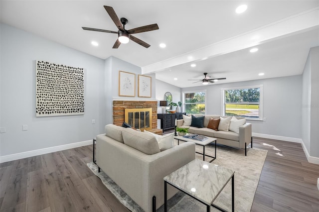 living room with wood-type flooring, a stone fireplace, and ceiling fan