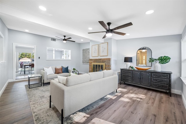 living room with a stone fireplace, ceiling fan, and dark hardwood / wood-style floors