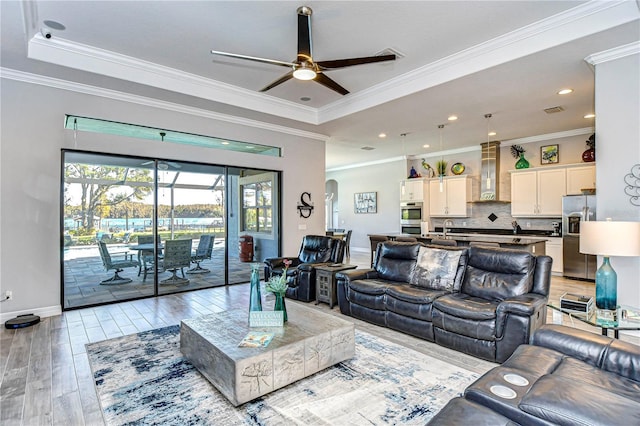 living room with sink, crown molding, ceiling fan, a tray ceiling, and light hardwood / wood-style floors