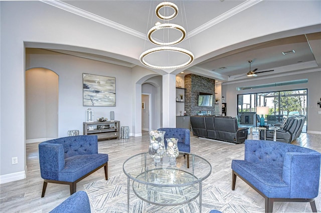 living room featuring ceiling fan, light wood-type flooring, ornamental molding, and a tray ceiling