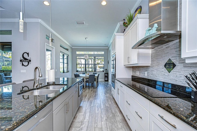 kitchen featuring white cabinets, dark stone countertops, wall chimney range hood, and sink