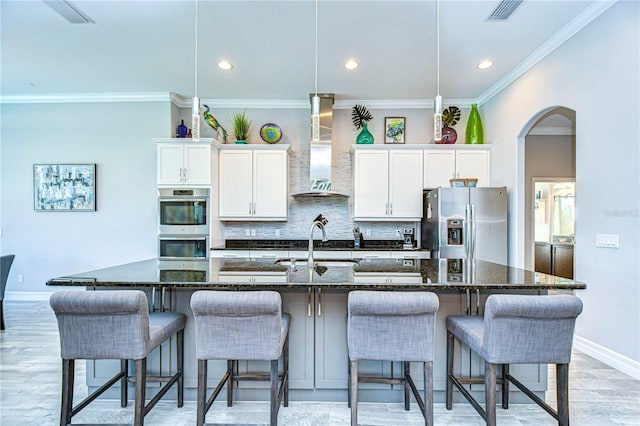 kitchen with a kitchen bar, a large island with sink, stainless steel appliances, and wall chimney exhaust hood