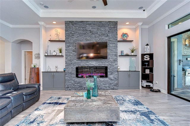 living room with crown molding, light hardwood / wood-style flooring, built in shelves, ceiling fan, and a fireplace