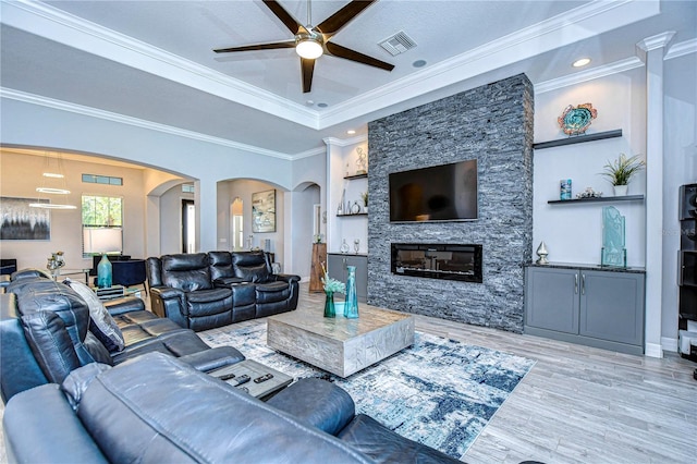 living room with a stone fireplace, ceiling fan, ornamental molding, built in features, and light hardwood / wood-style floors